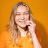 A smiling woman eats chips in front of an orange background.
