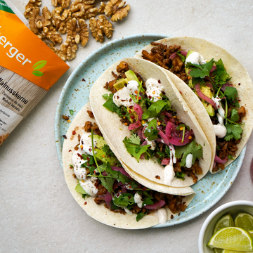 Tacos gefüllt mit Gemüse und Nüssen, serviert auf einem Teller neben geschnittenen Limetten.