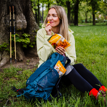 Frau sitzt mit Rucksack auf Gras und isst Mango