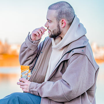 Eine Person isst einen Snack und sitzt draußen nah am Wasser.
