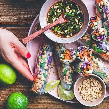 Vietnamesische Frühlingsrollen liegen auf einem Teller mit Sojasoße und Limetten daneben.