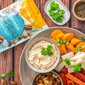 Ein Teller mit Gemüsesticks und Dip neben einer Packung Seeberger Nusssnack.